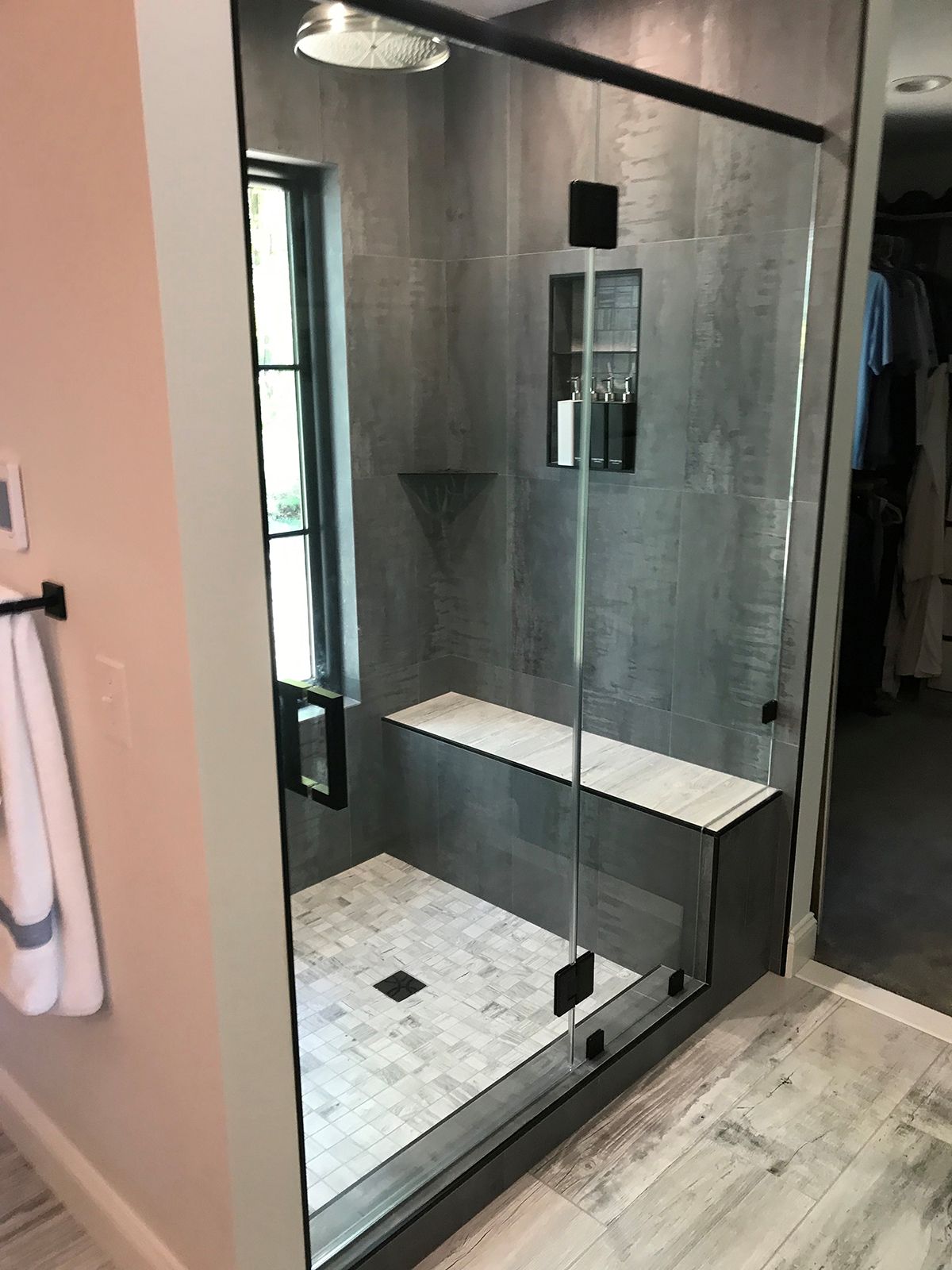 A walk-in shower with a glass door, grey tiled walls, a tiled bench, and a small recessed shelf.