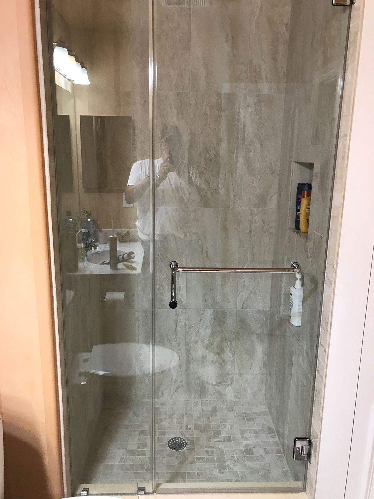 A frameless glass shower door with a horizontal silver handle, set against tiled walls and a stone-tiled shower floor.