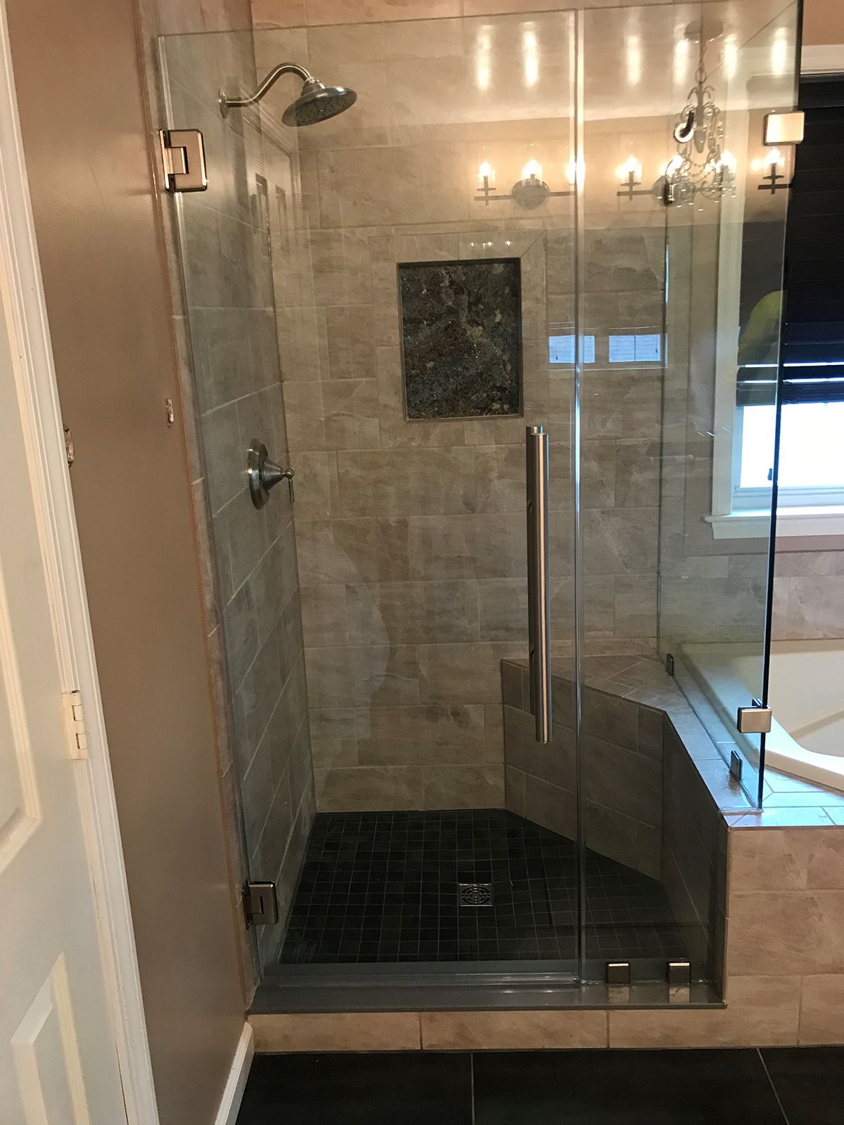 A glass shower enclosure with beige tiled walls, a black pebble floor, a built-in corner seat, and a chrome showerhead.