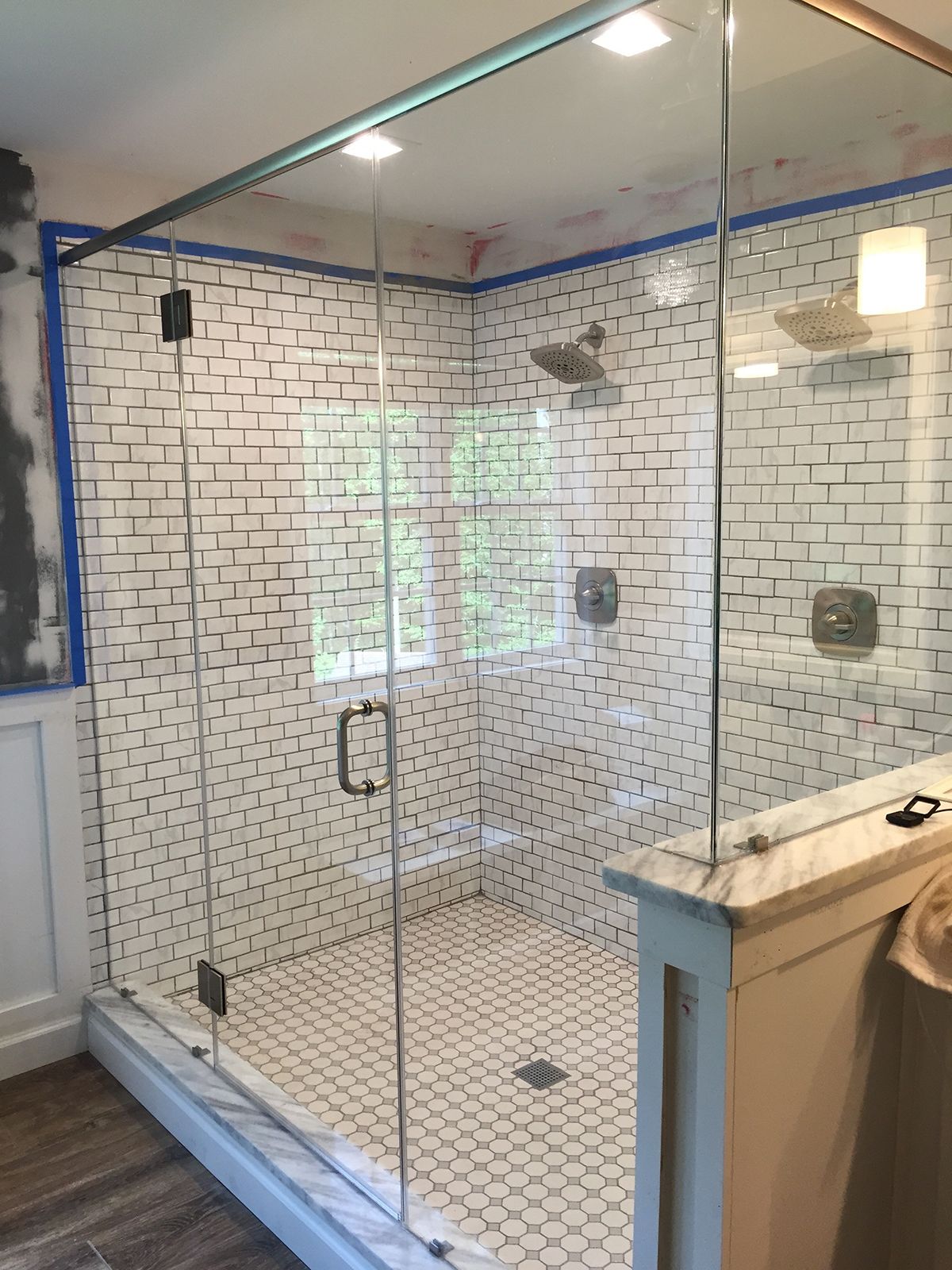 A modern glass-enclosed shower with white subway tile walls and patterned floor tile.