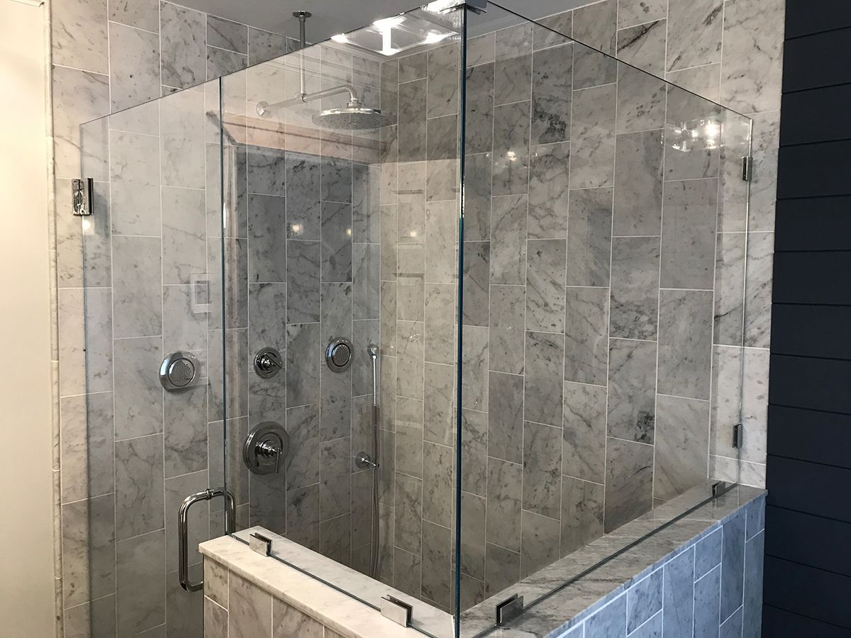 A walk-in shower with clear glass panels, chrome fixtures, and light gray marble tile walls.
