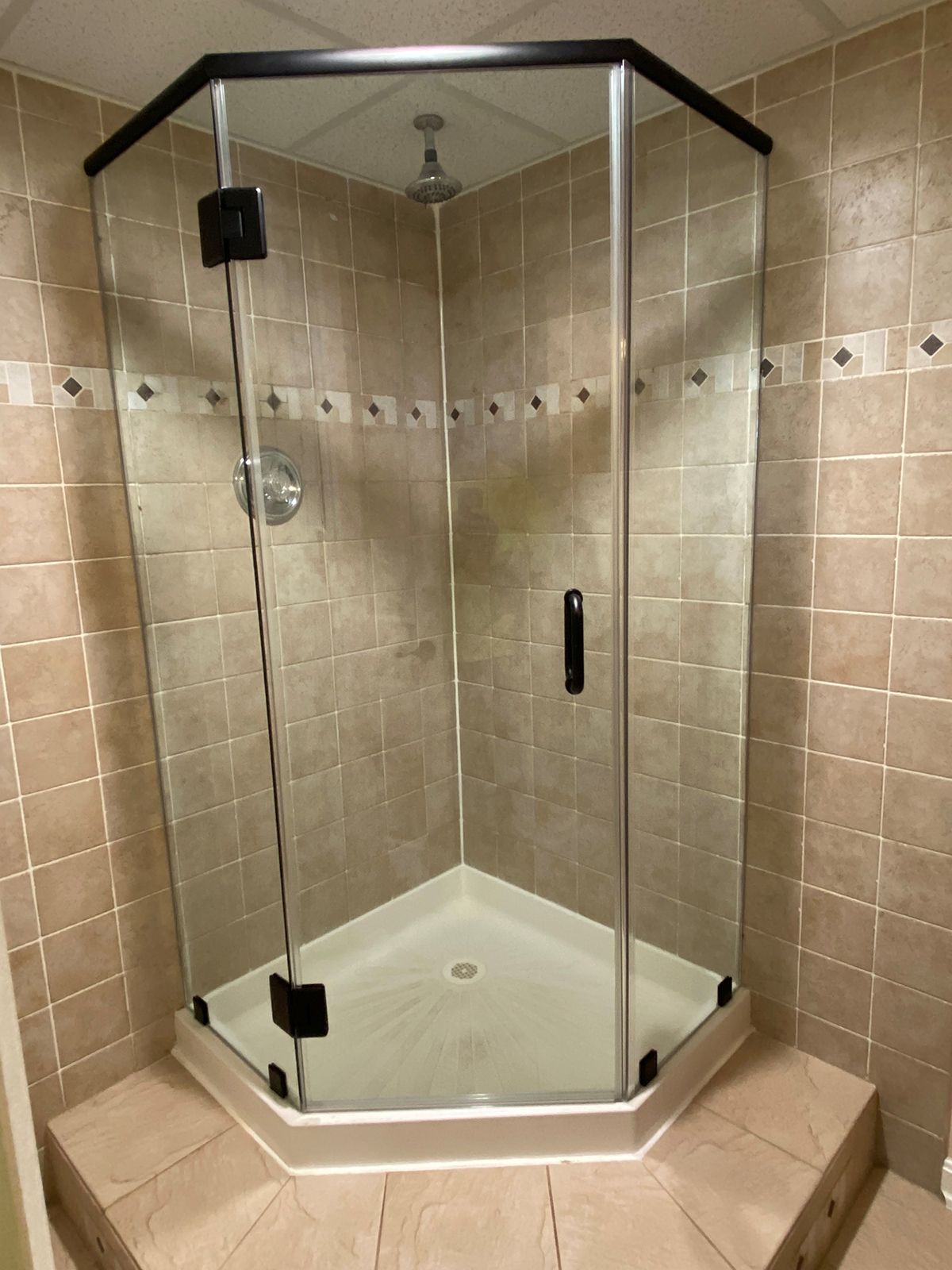 A glass neo-angle shower enclosure with black frames, set in a corner with beige tiled walls and a white floor base.