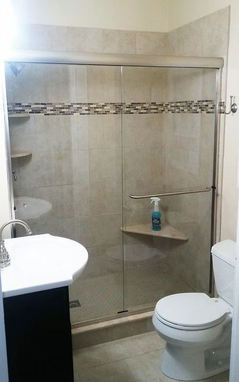 A small bathroom with a glass-enclosed shower, a white pedestal sink, and a white toilet on beige tiled flooring.