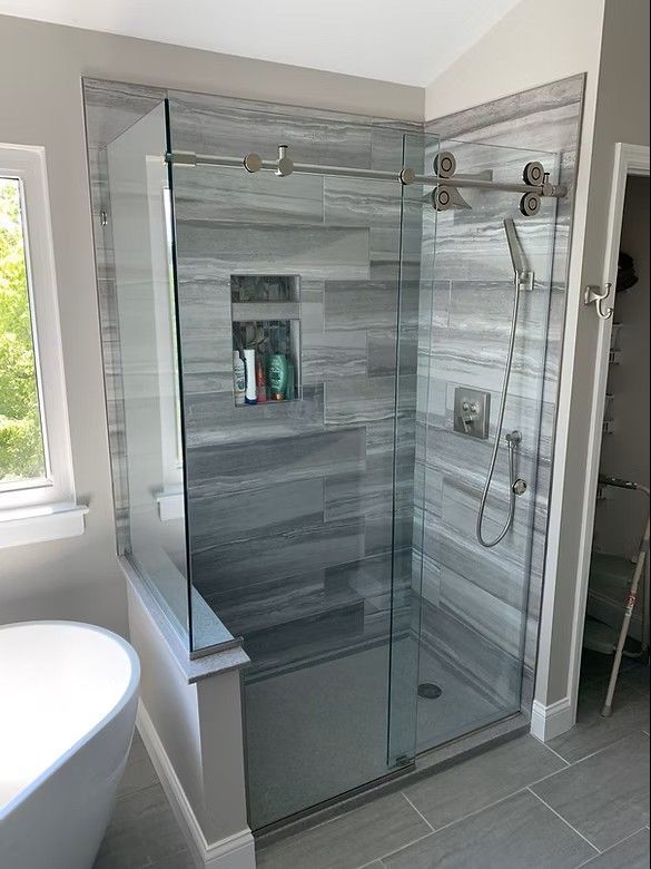 A modern walk-in shower with grey horizontal tile walls, a built-in niche, glass sliding doors, and a handheld sprayer.