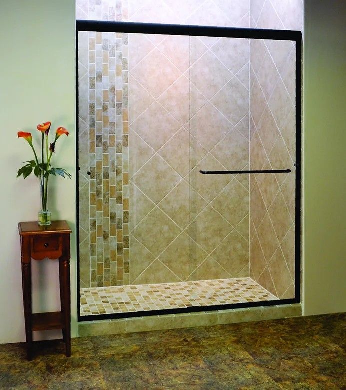 A glass shower enclosure with a black frame, featuring tiled walls and a mosaic floor, next to a small wooden table.