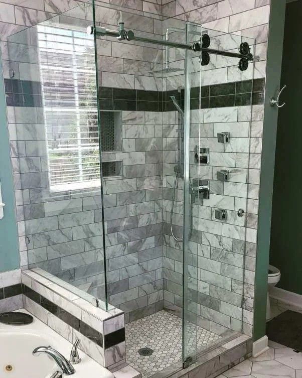A modern glass-enclosed shower with gray and white marble subway tile walls, a rain showerhead, and a mosaic tile floor.