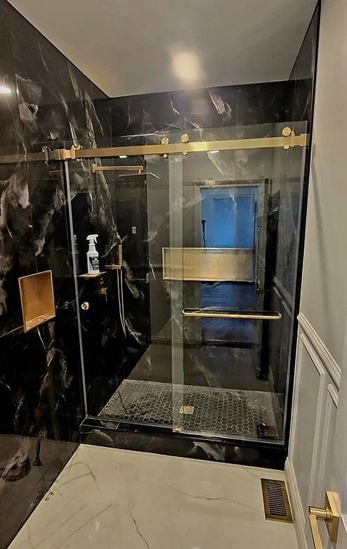 Gold-framed glass shower with black marble walls, gold fixtures, and gray flooring.