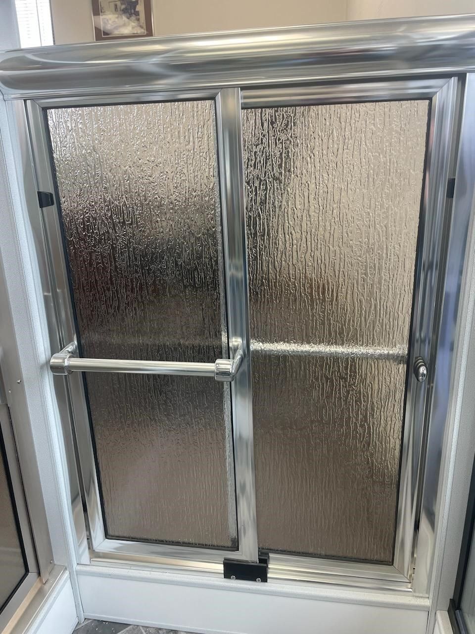Silver-framed shower door with textured glass. Chrome towel bars and frame against white shower walls.