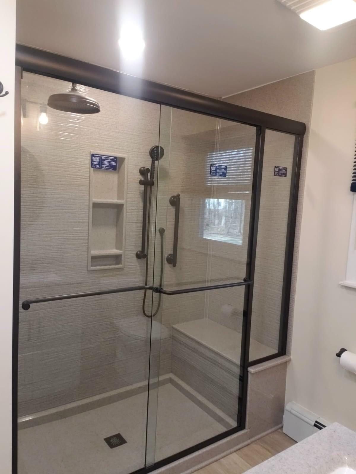 Modern shower with glass doors, dark trim, and built-in bench. Features showerhead, handheld, and grab bar.