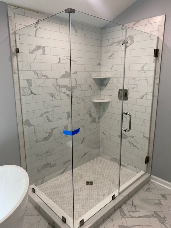 Glass shower enclosure with white marble tile walls and herringbone tile floor.