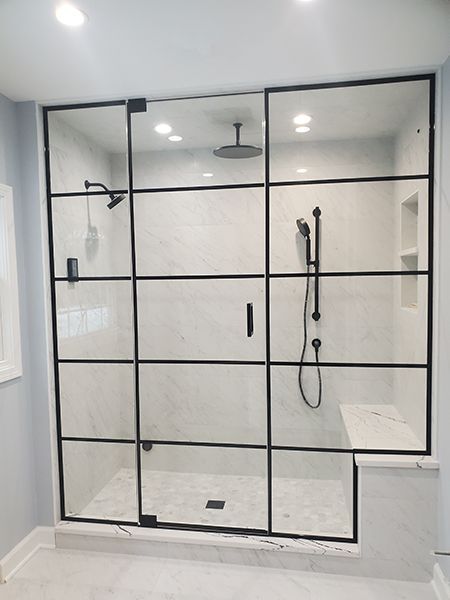 Glass shower enclosure with stone tile and a bathtub in a bathroom.