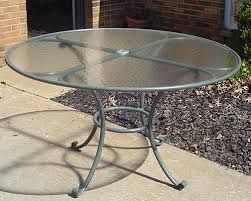 Round metal patio table with a glass top, on a concrete patio.