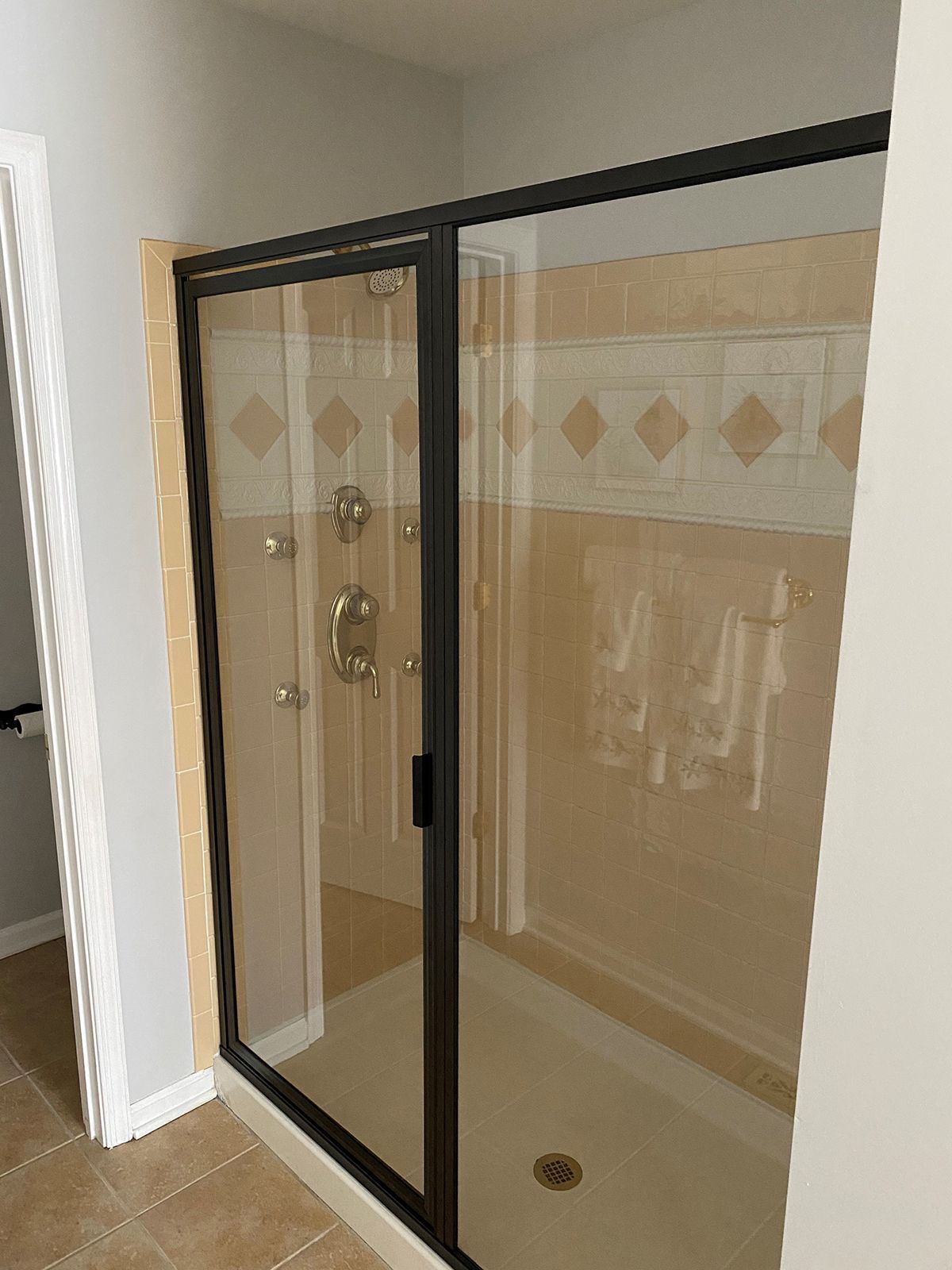 A shower enclosure with black metal framing and a glass door, set against a tiled bathroom wall with a decorative inlay.