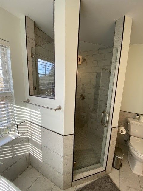 Bathroom with glass shower, toilet, and window with blinds.