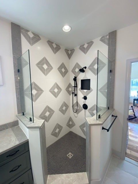 A modern shower with geometric tile design, glass dividers, and black fixtures.