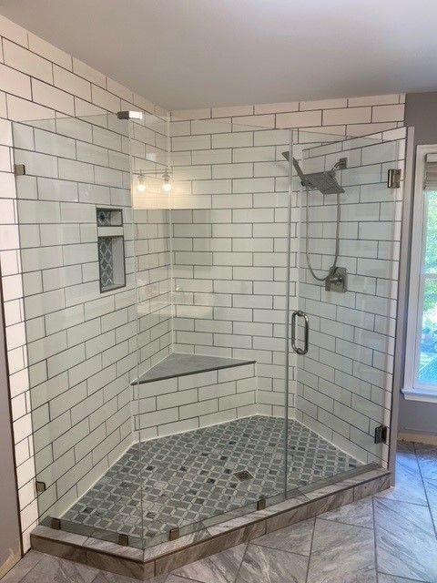Corner shower with white subway tile walls, glass doors, and gray mosaic tile floor.