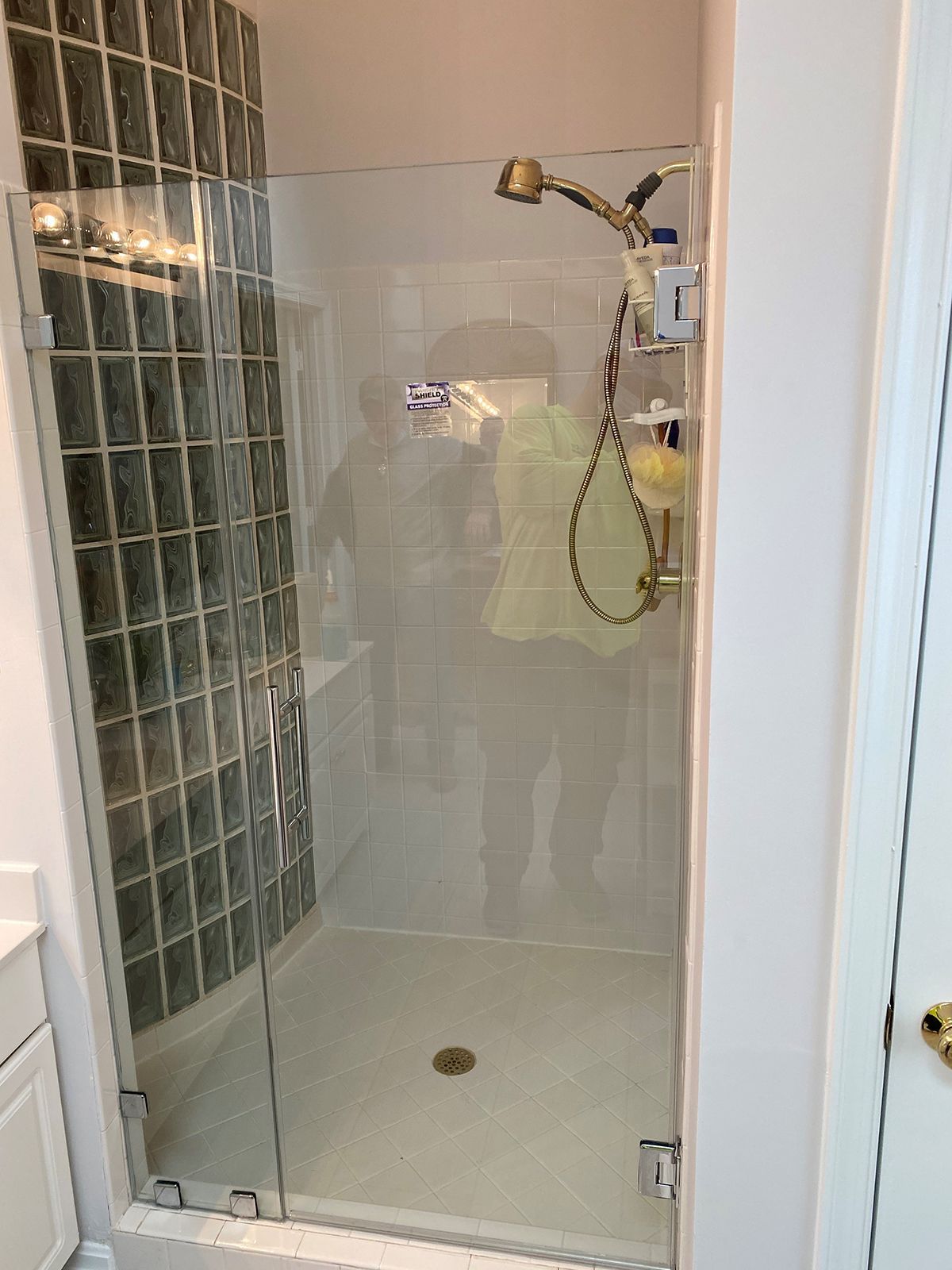 A glass-enclosed shower with a gold handheld showerhead fixture and glass block tile wall.