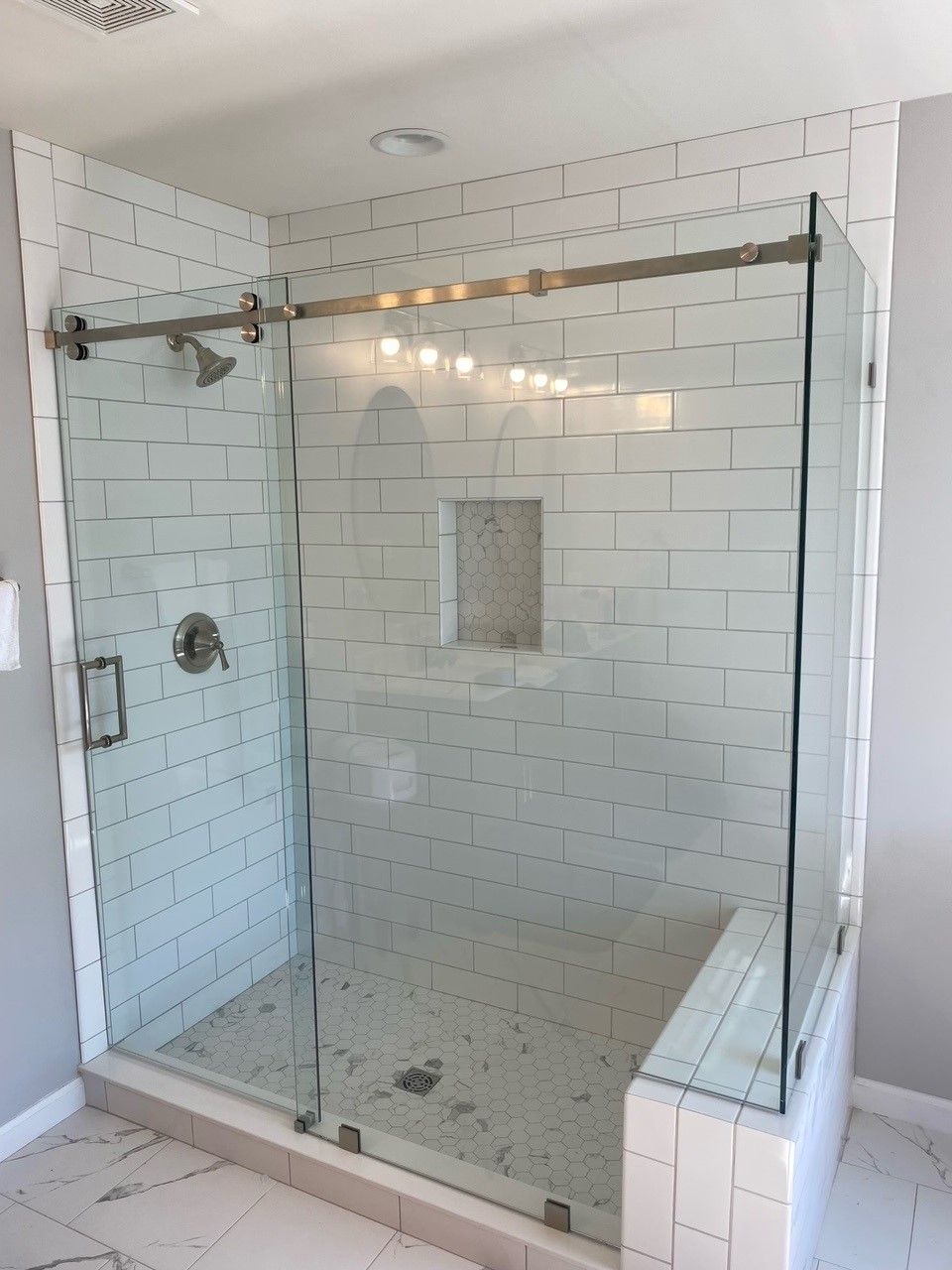 Modern white-tiled shower with glass doors, a silver showerhead, and a built-in shelf.