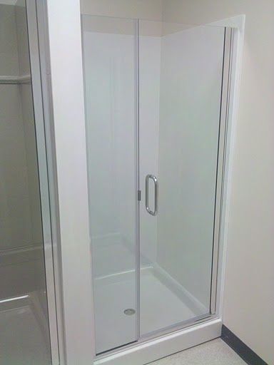 Glass shower enclosure with sliding door and metal handle in a white-walled room.