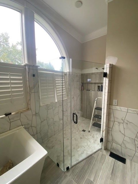 Bathroom with marble-like tile, glass shower door, and a white soaking tub.