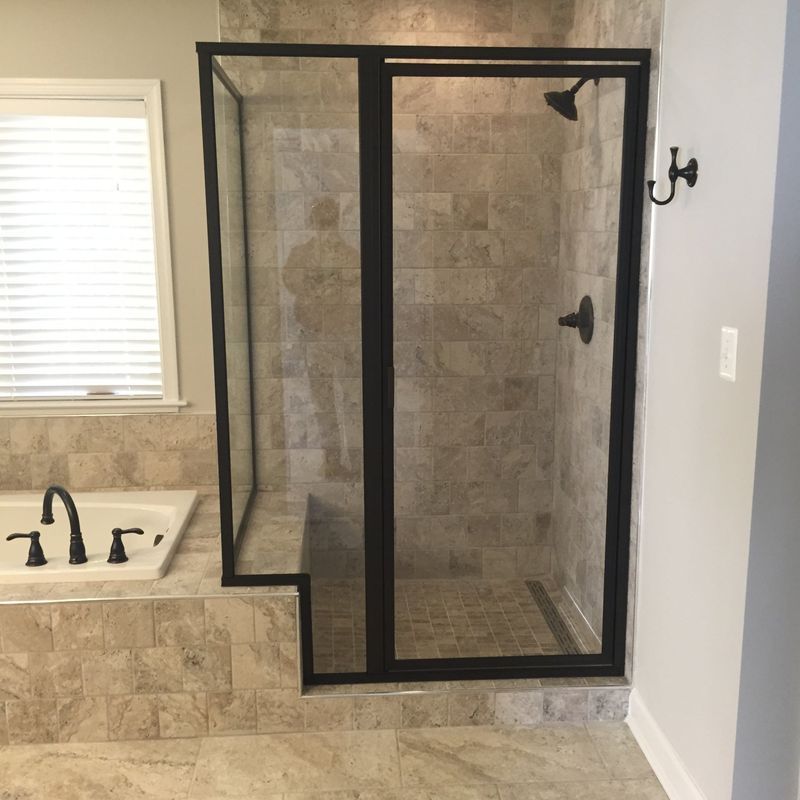 Bathroom with glass shower enclosure, beige tile, black fixtures, and window with blinds.