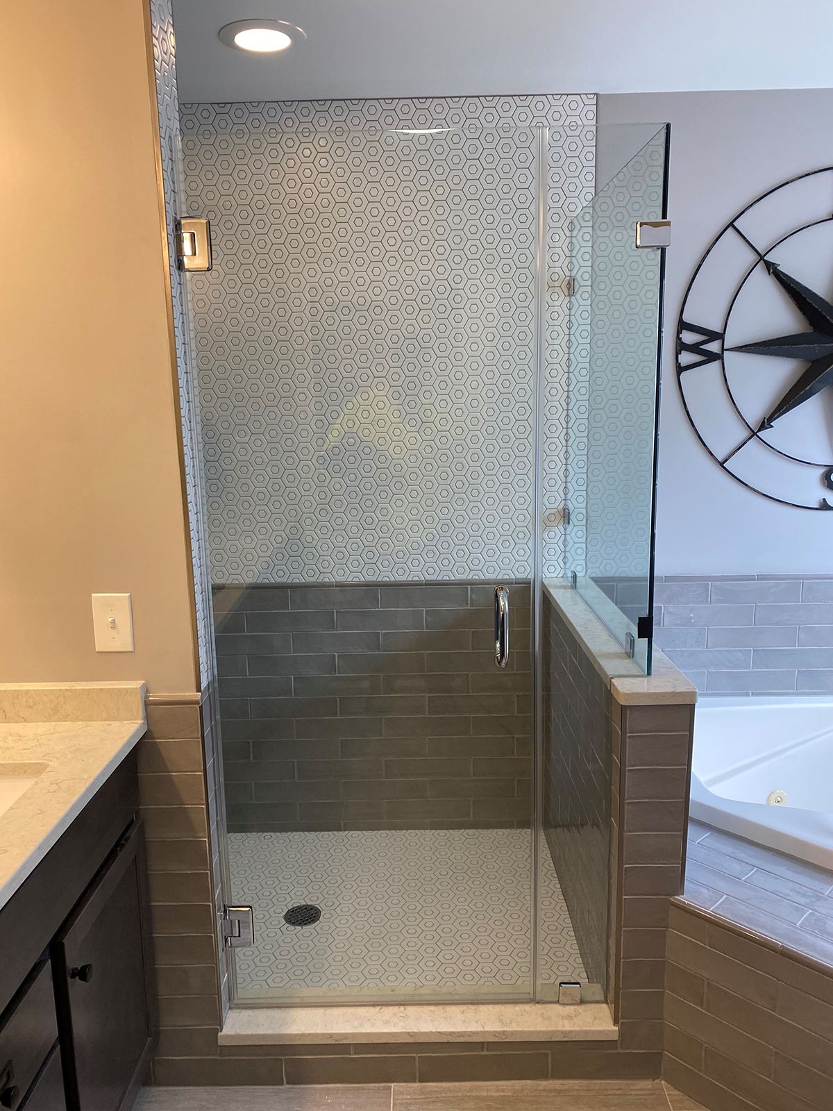 A modern walk-in shower with a glass door, light pebble floor, mosaic tile wall, and brown subway tile base.