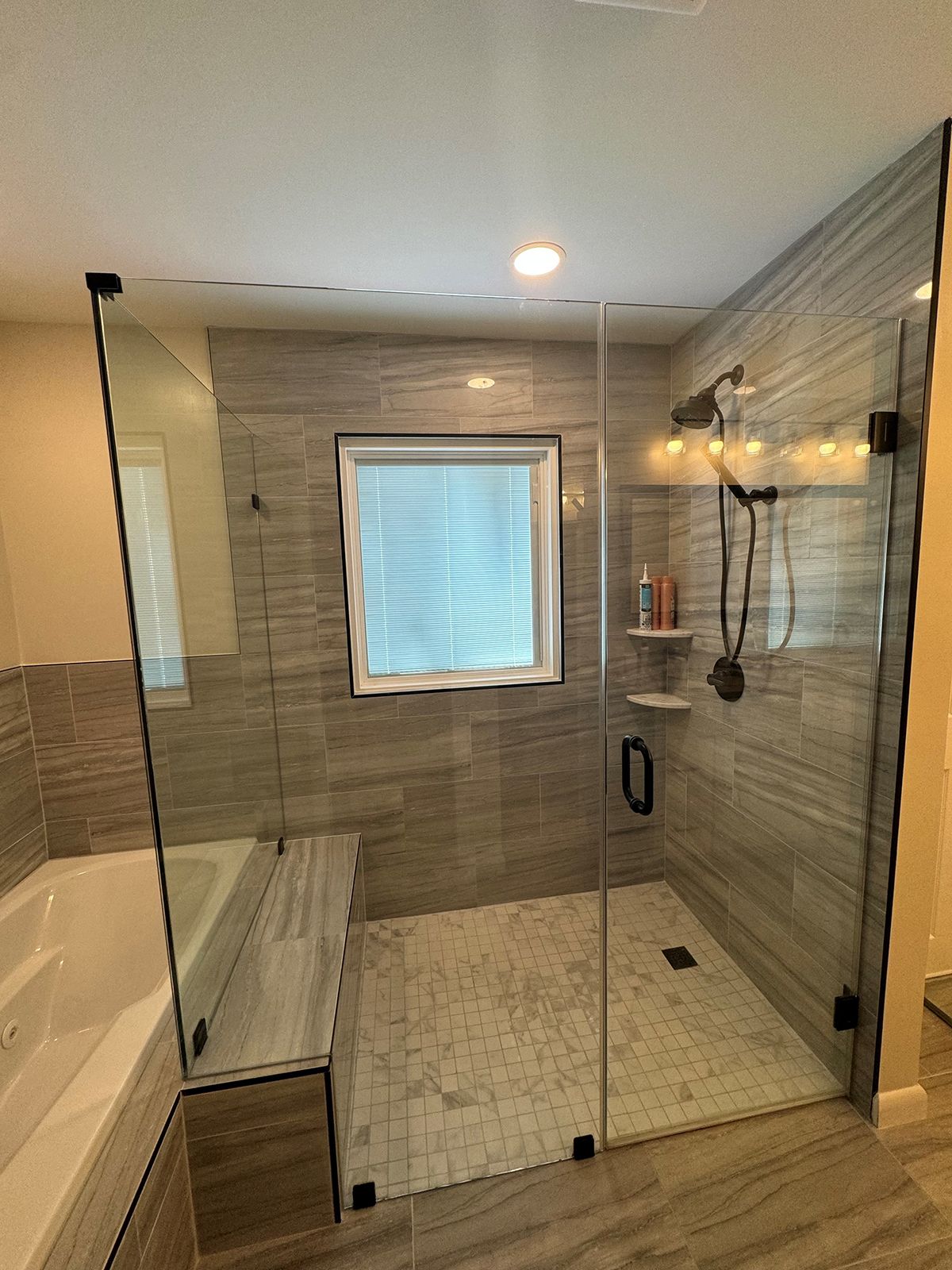 Modern bathroom featuring a tiled walk-in shower with glass doors, a built-in bench, and an adjacent soaking tub.