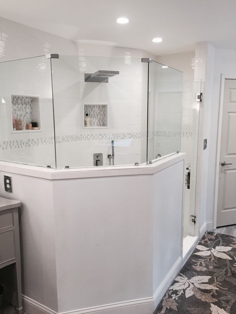 Modern bathroom with glass shower enclosure, white tile walls, and gray vanity.