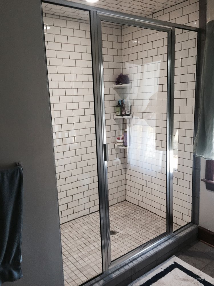Shower with glass doors and white subway tile walls. A shelf holds toiletries. Grey towel on the left.