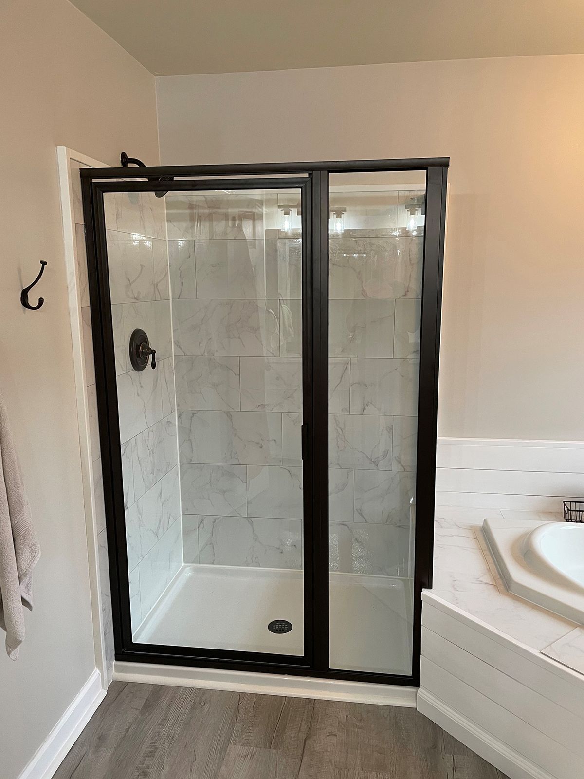 A modern shower stall featuring white marble-patterned tiles, a white shower pan, and a black metal frame glass door.