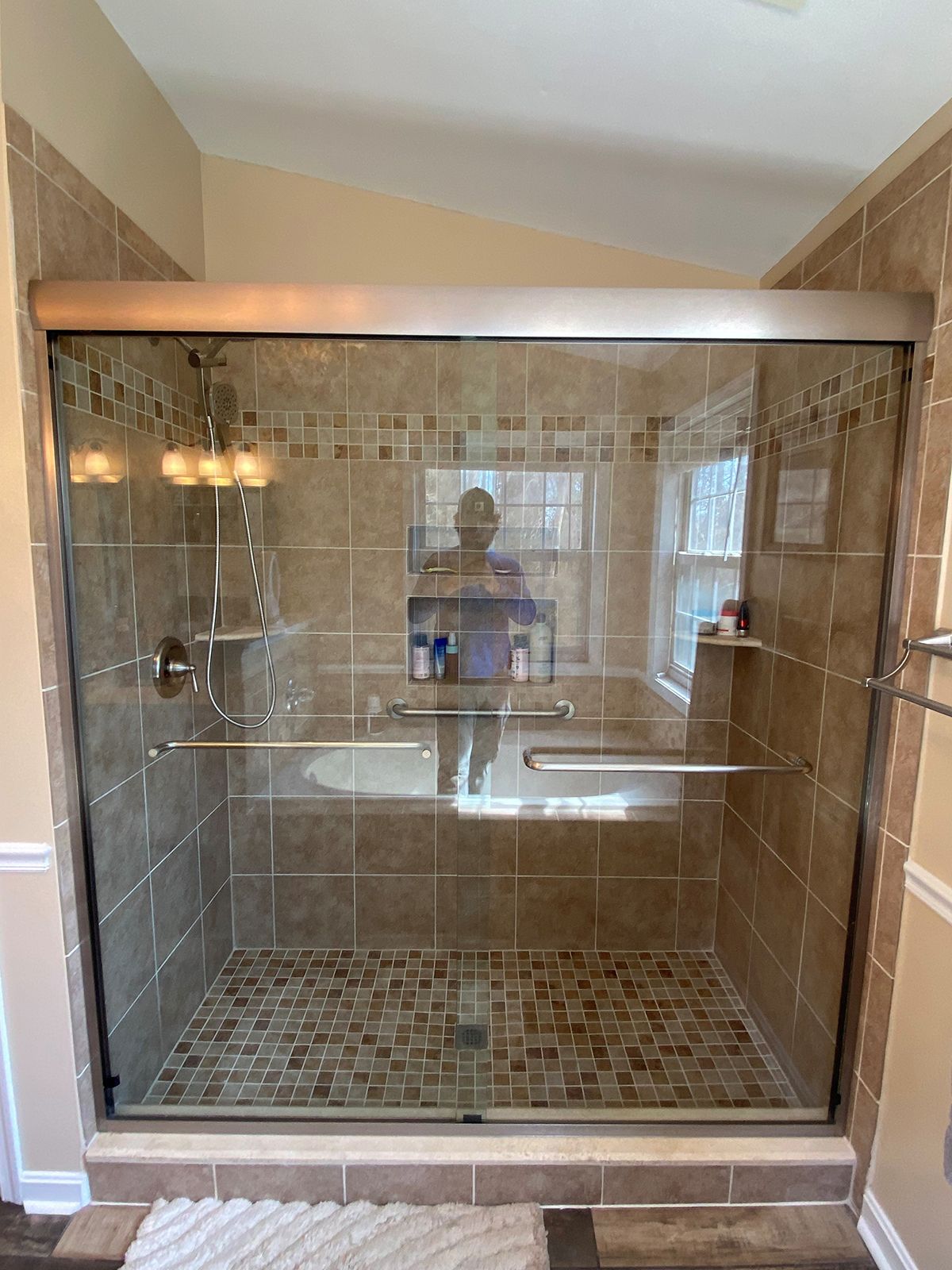 A tiled walk-in shower with a glass door, metal frame, and interior shelves, reflecting a bathroom interior.