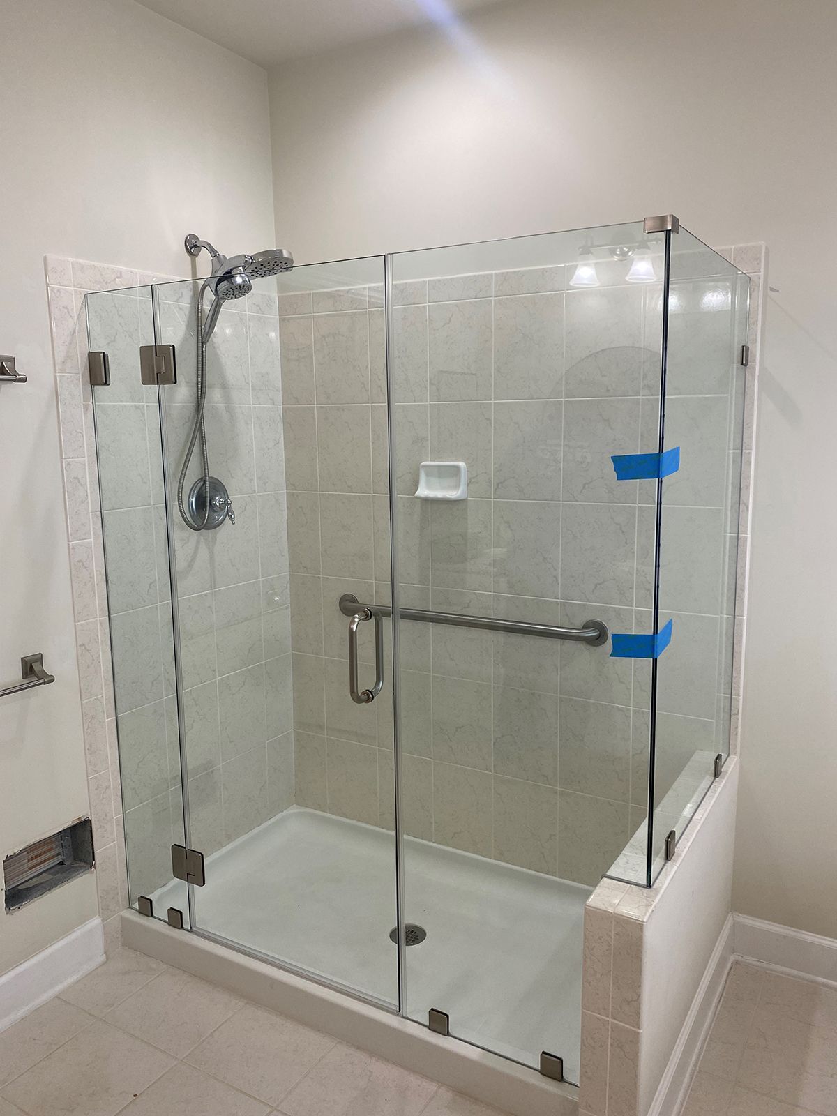 A walk-in shower with a glass enclosure, chrome fixtures, and blue painter's tape on the door frame.