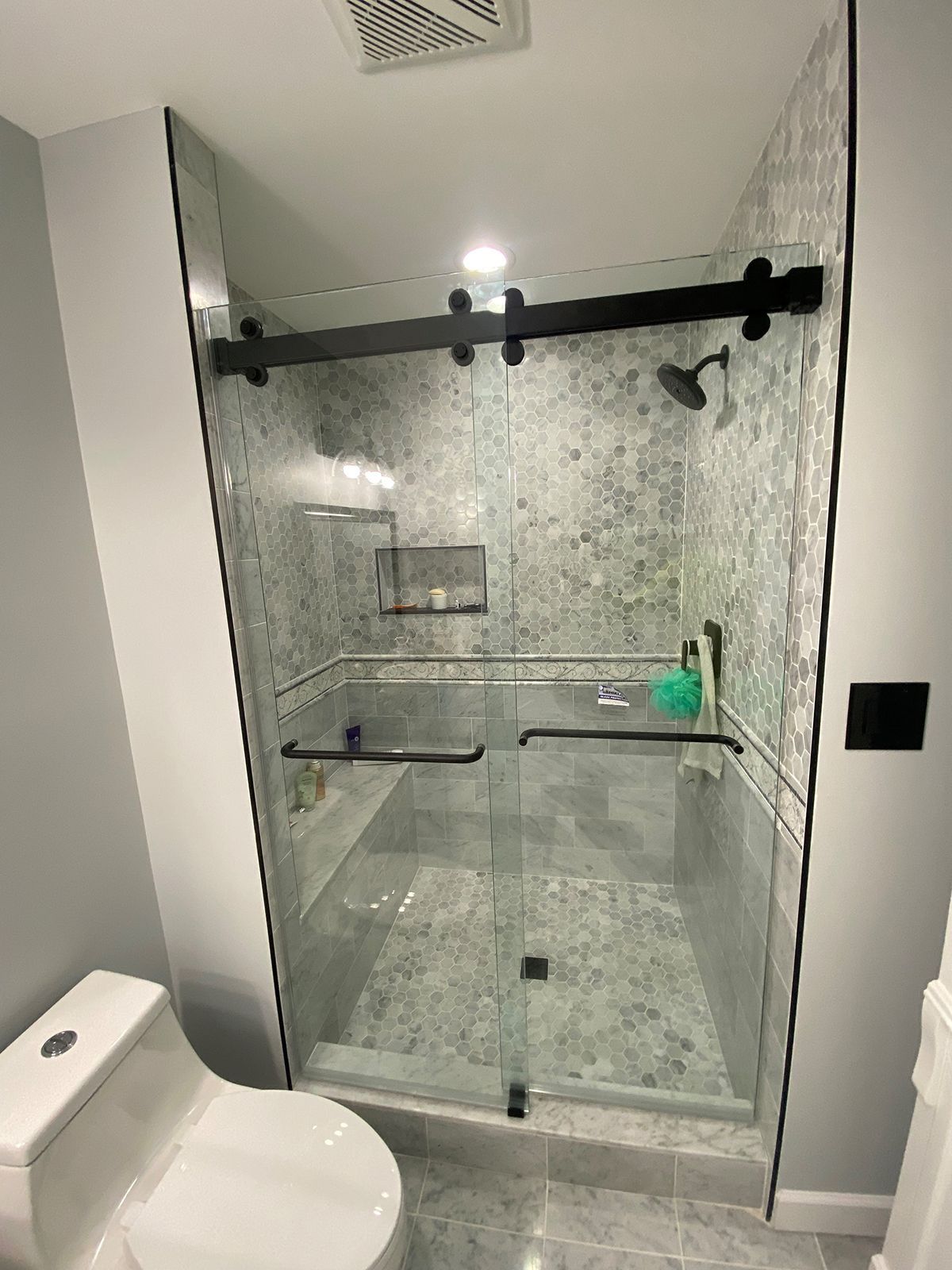 A modern glass-enclosed shower with matte black hardware, sliding doors, and patterned tile walls next to a toilet.