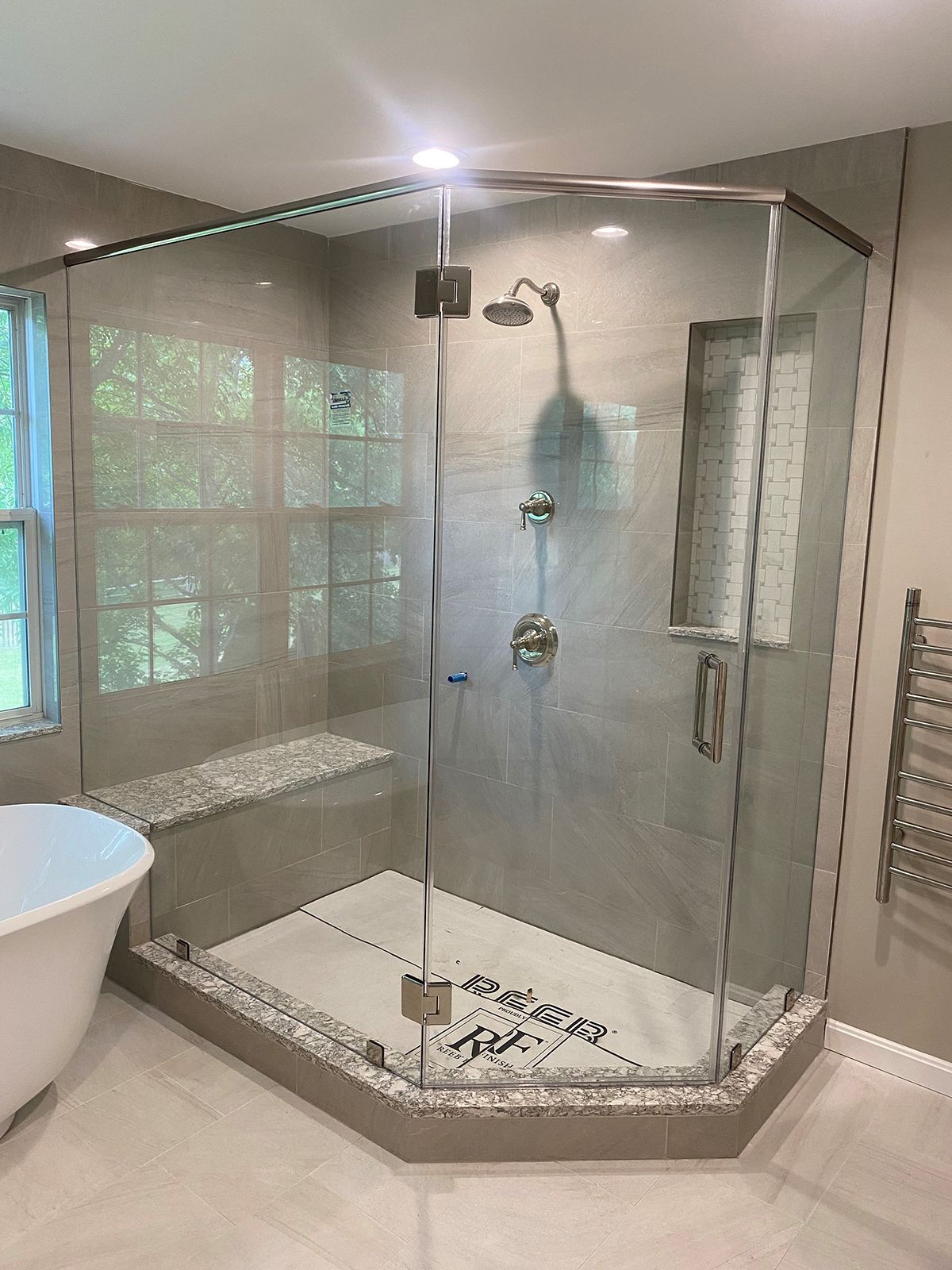 A modern walk-in shower with glass walls, a built-in stone bench, gray tile, and a handheld chrome shower fixture.