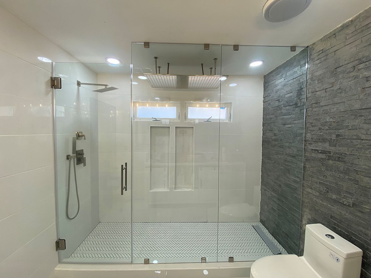 A glass-enclosed shower with a patterned tile floor next to a dark, textured stone wall in a modern bathroom.