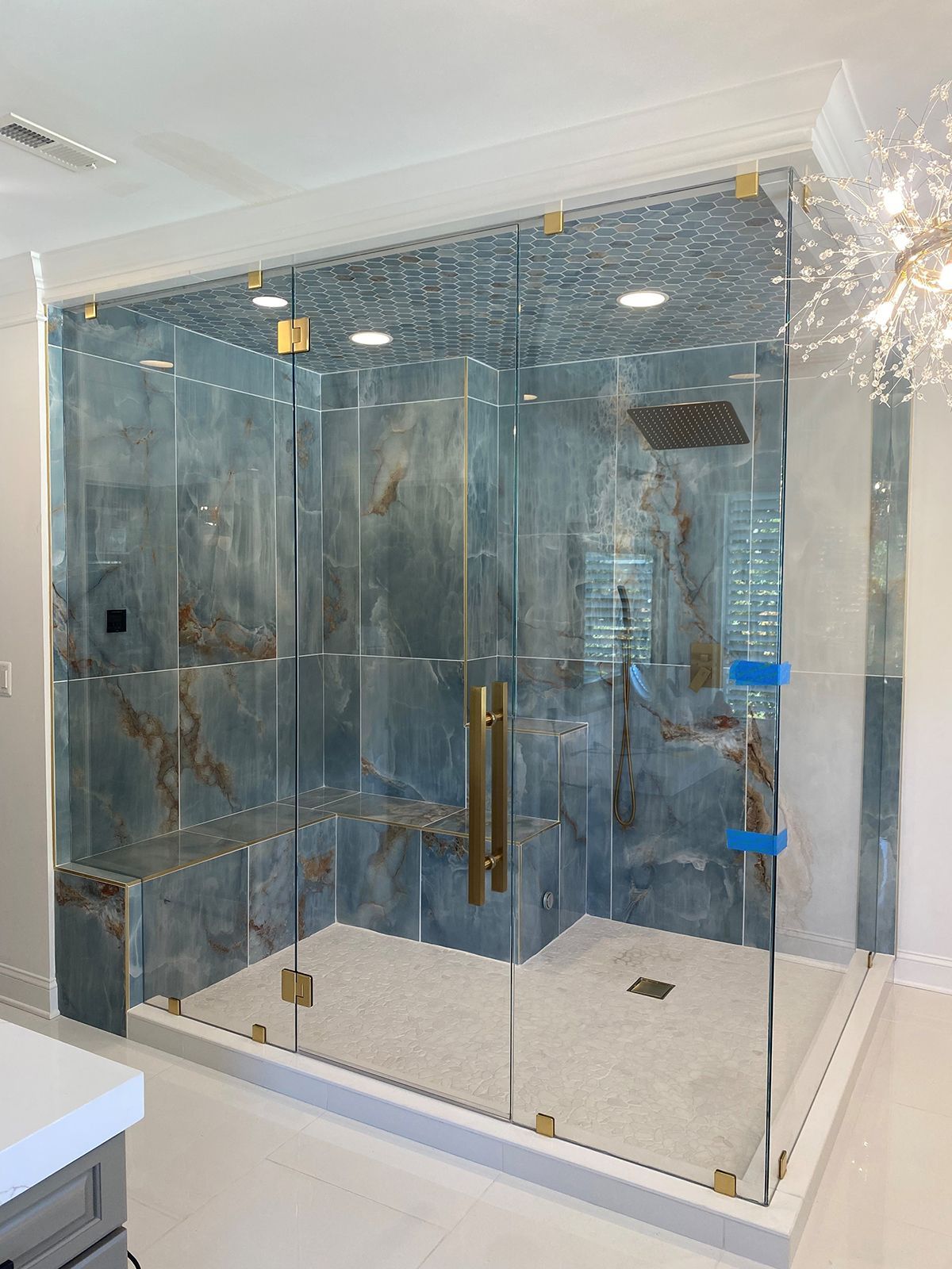 A walk-in shower with blue marble-patterned tiles, a built-in bench, and gold hardware behind a glass enclosure.
