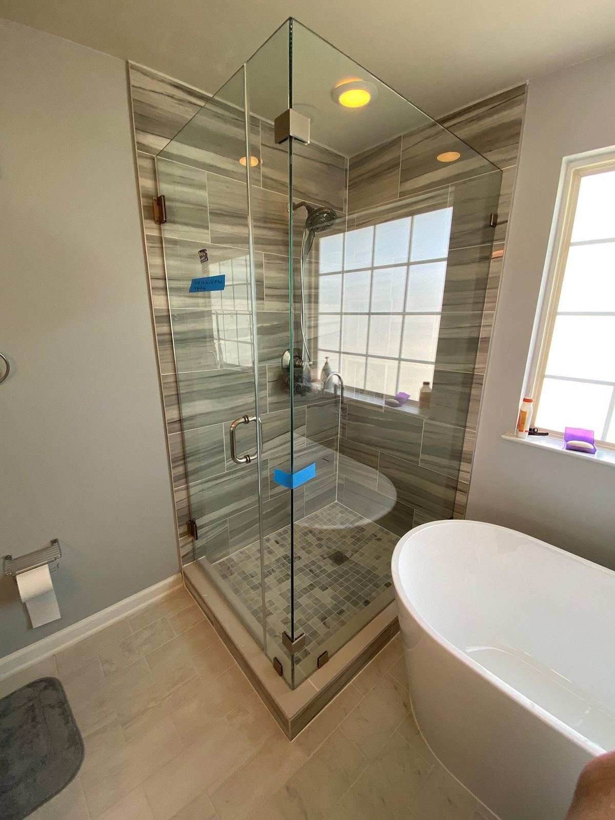 A modern bathroom featuring a glass-enclosed shower with grey tiled walls, positioned next to a white soaking tub.