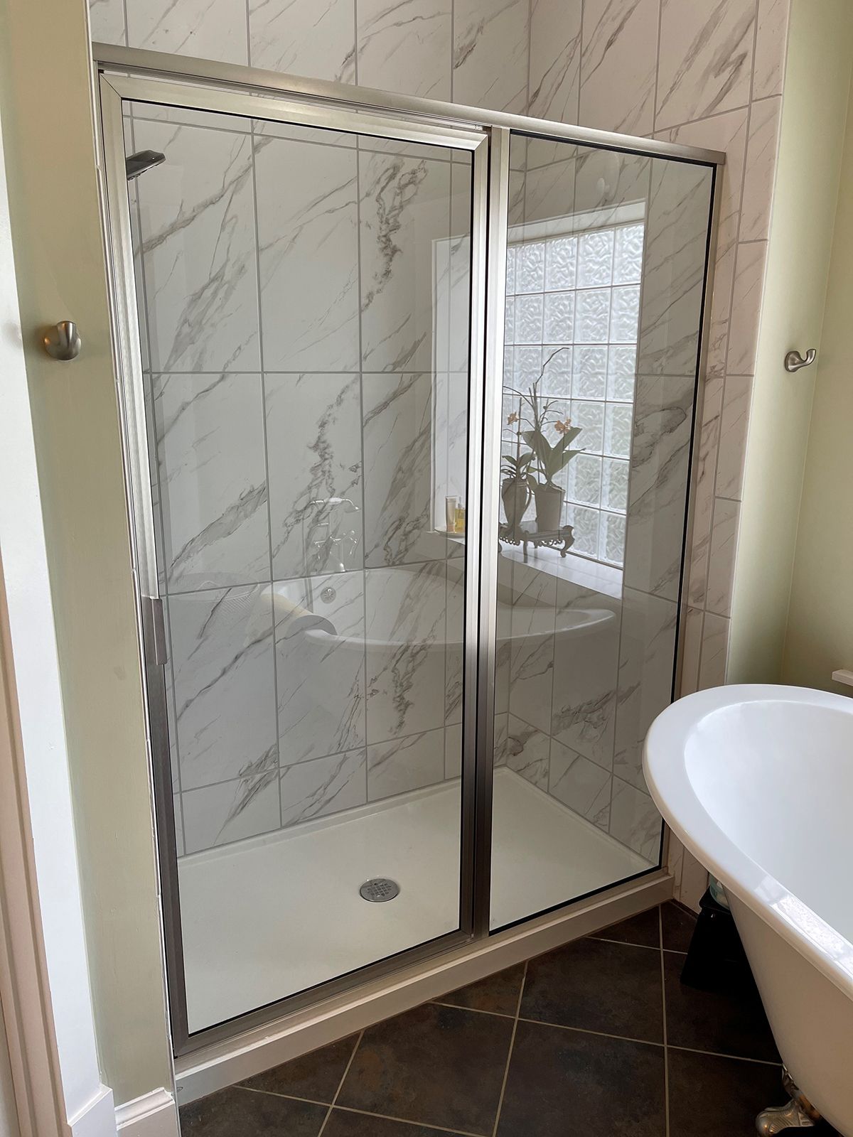 A walk-in shower with chrome-framed glass doors and marble-patterned tile, positioned next to a white freestanding tub.
