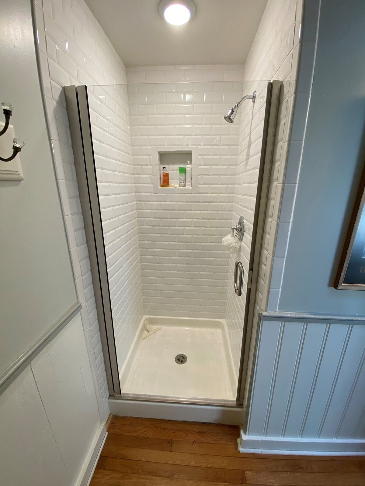 A white subway-tiled walk-in shower with a glass door, a built-in shampoo niche, and a chrome showerhead.