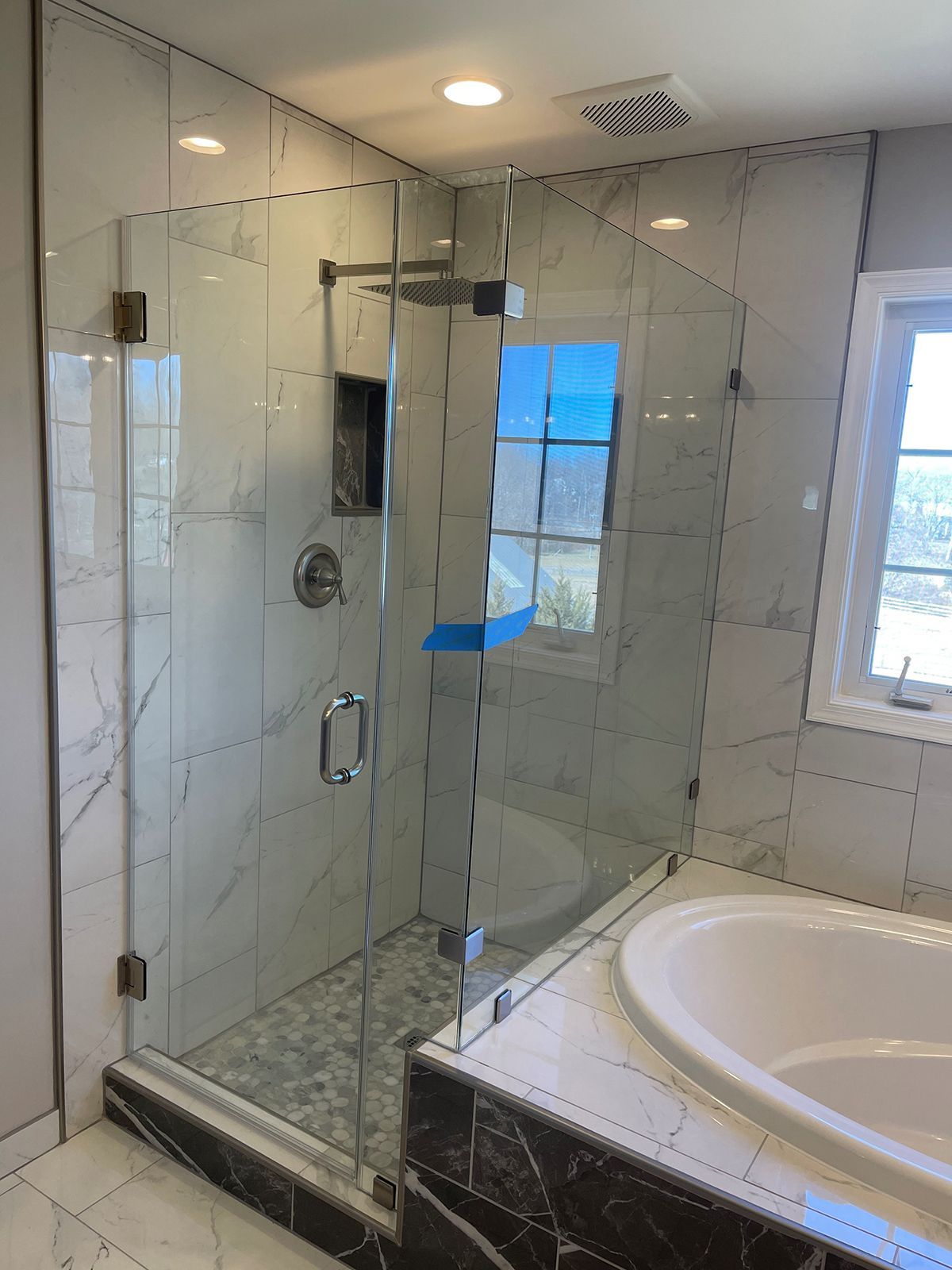 A glass-enclosed shower with white marble-patterned tiles and a pebble floor, adjacent to a white soaking tub.