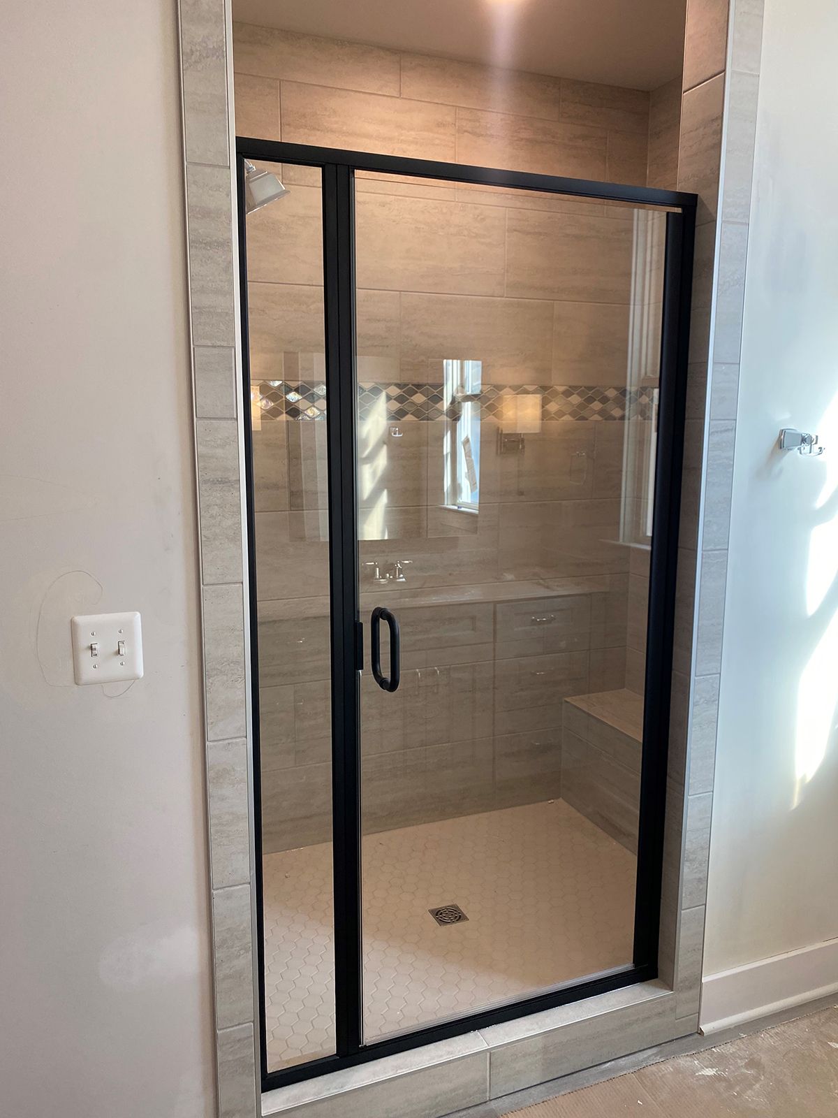 A modern walk-in shower with a black-framed glass door, tiled walls, and a small built-in bench.