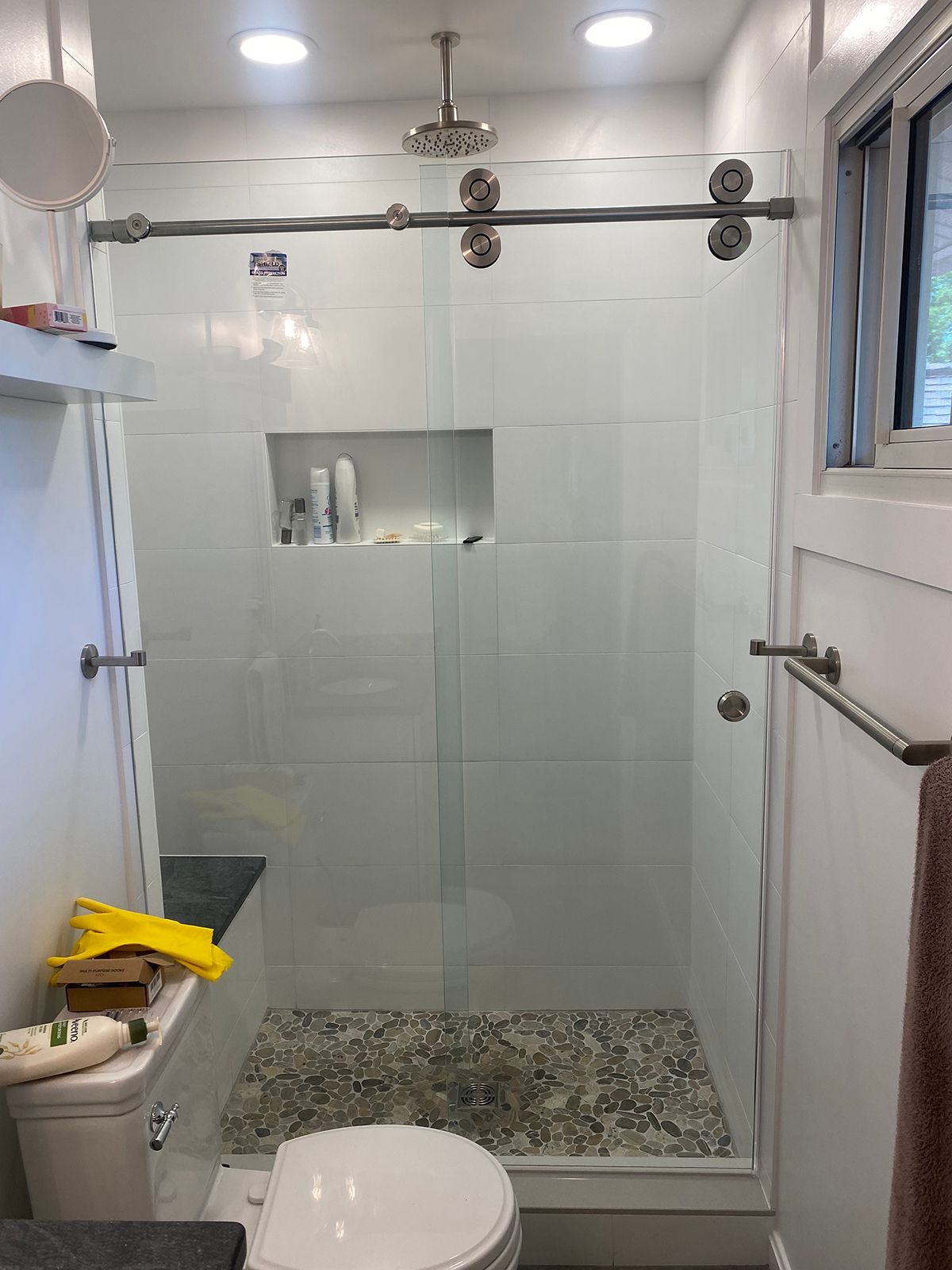 A bathroom shower with white tiled walls, a glass sliding door, a stone floor, and a built-in recessed shelf.