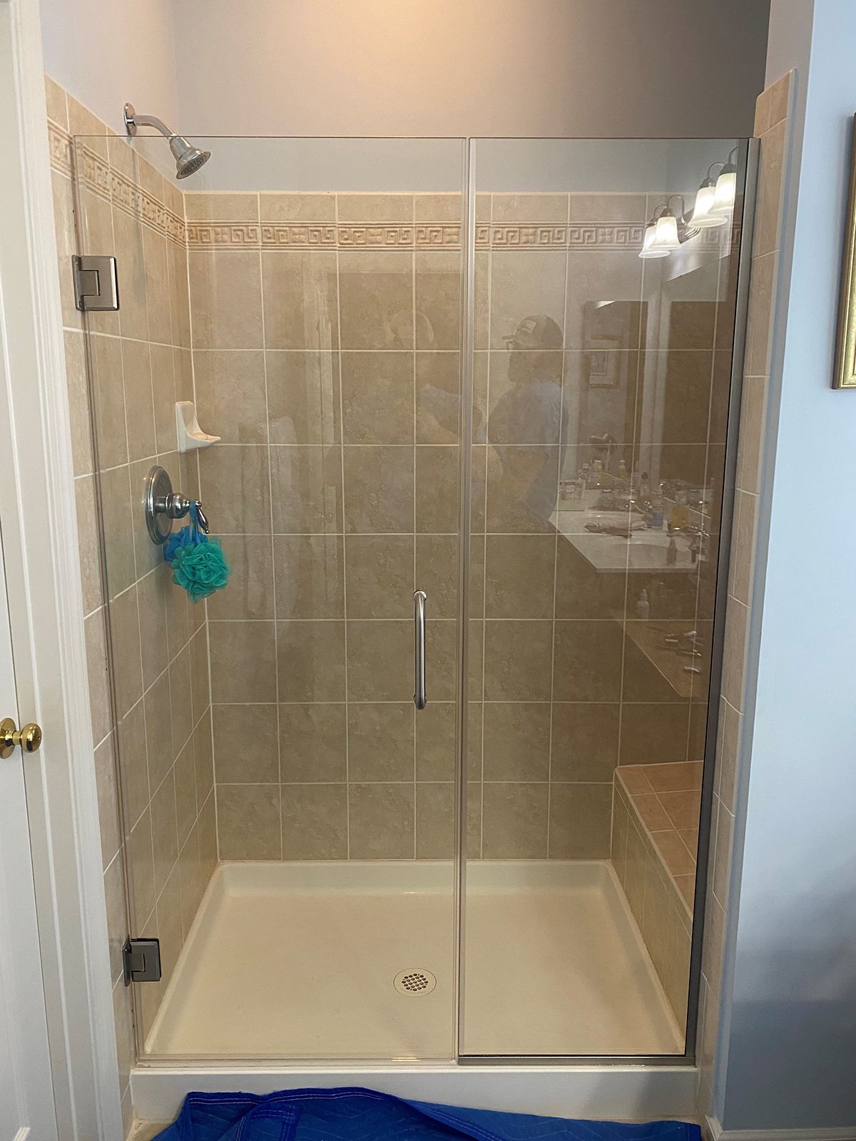 A glass shower enclosure with a hinged door and a tile interior against a light blue wall, with a blue mat at the base.