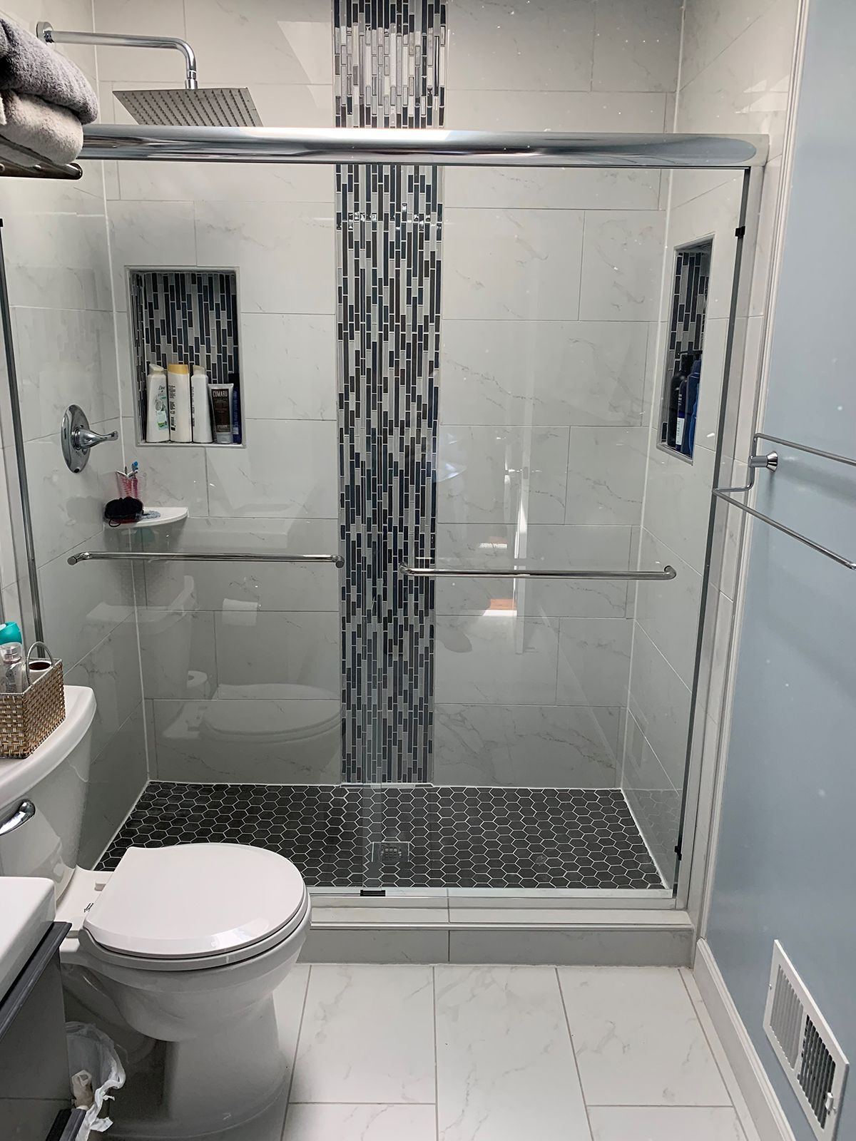 A modern bathroom featuring a walk-in glass shower with a black pebble floor and a vertical mosaic accent tile wall.