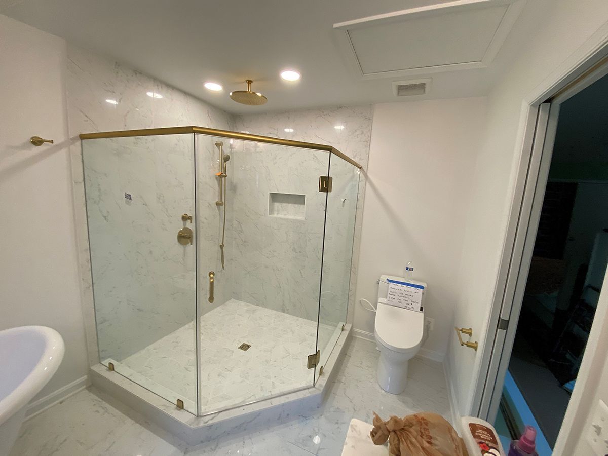 Modern bathroom with a glass-enclosed shower, gold fixtures, white marble tile, and a toilet next to an open doorway.