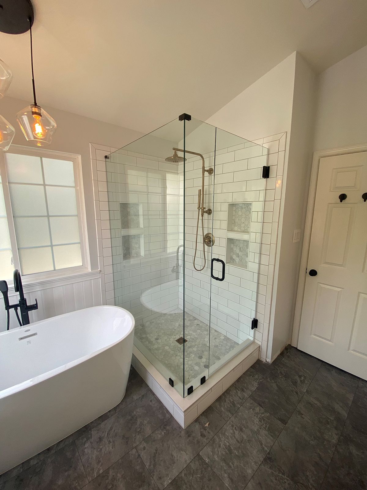 A white freestanding bathtub next to a glass-enclosed shower with white subway tiles in a modern bathroom.