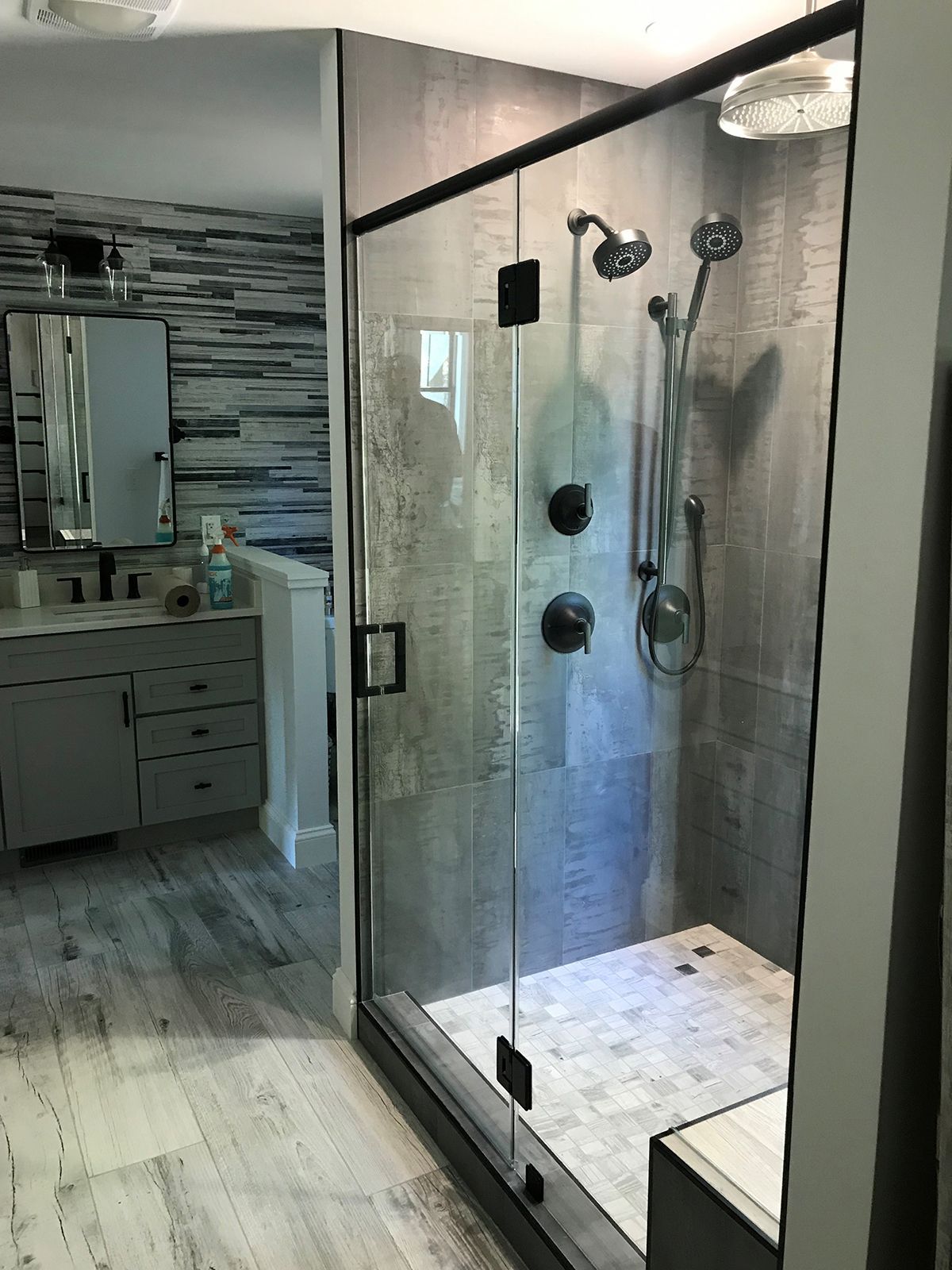 A modern bathroom featuring a glass-enclosed shower with a rainfall showerhead next to a grey vanity and striped walls.