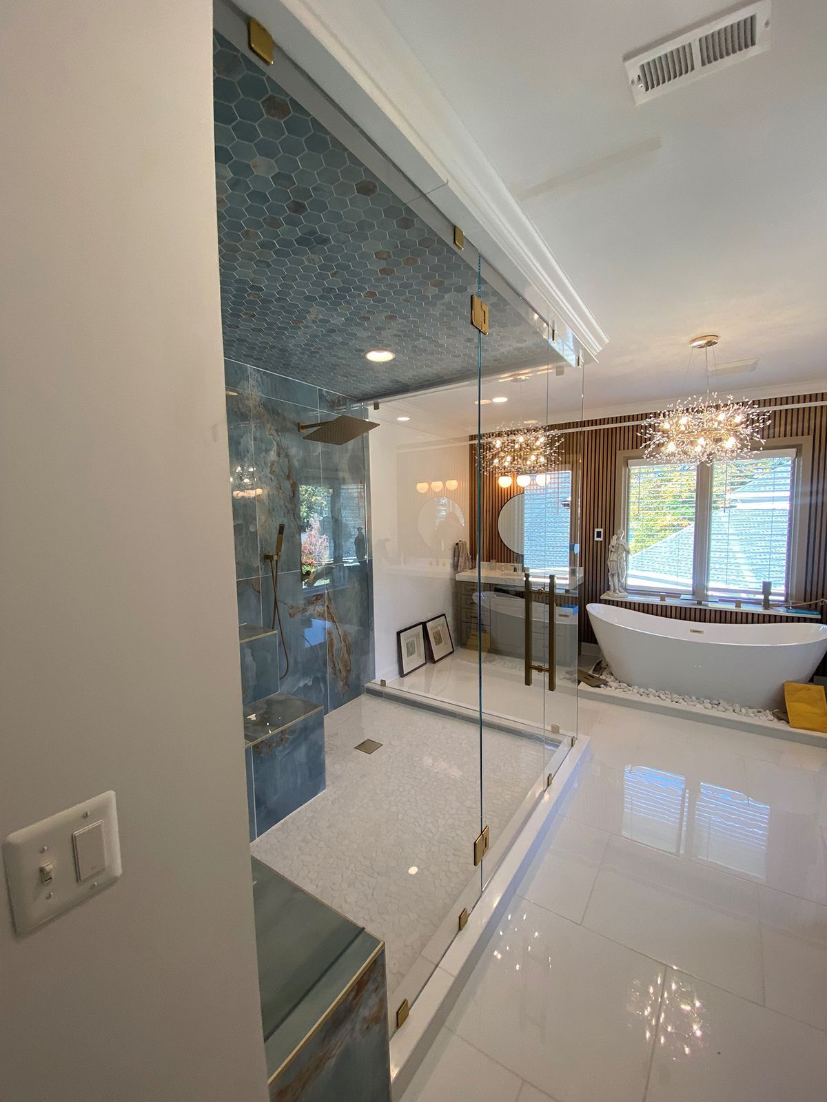 A modern bathroom with a glass-enclosed shower, a white soaking tub, and hanging chandeliers.