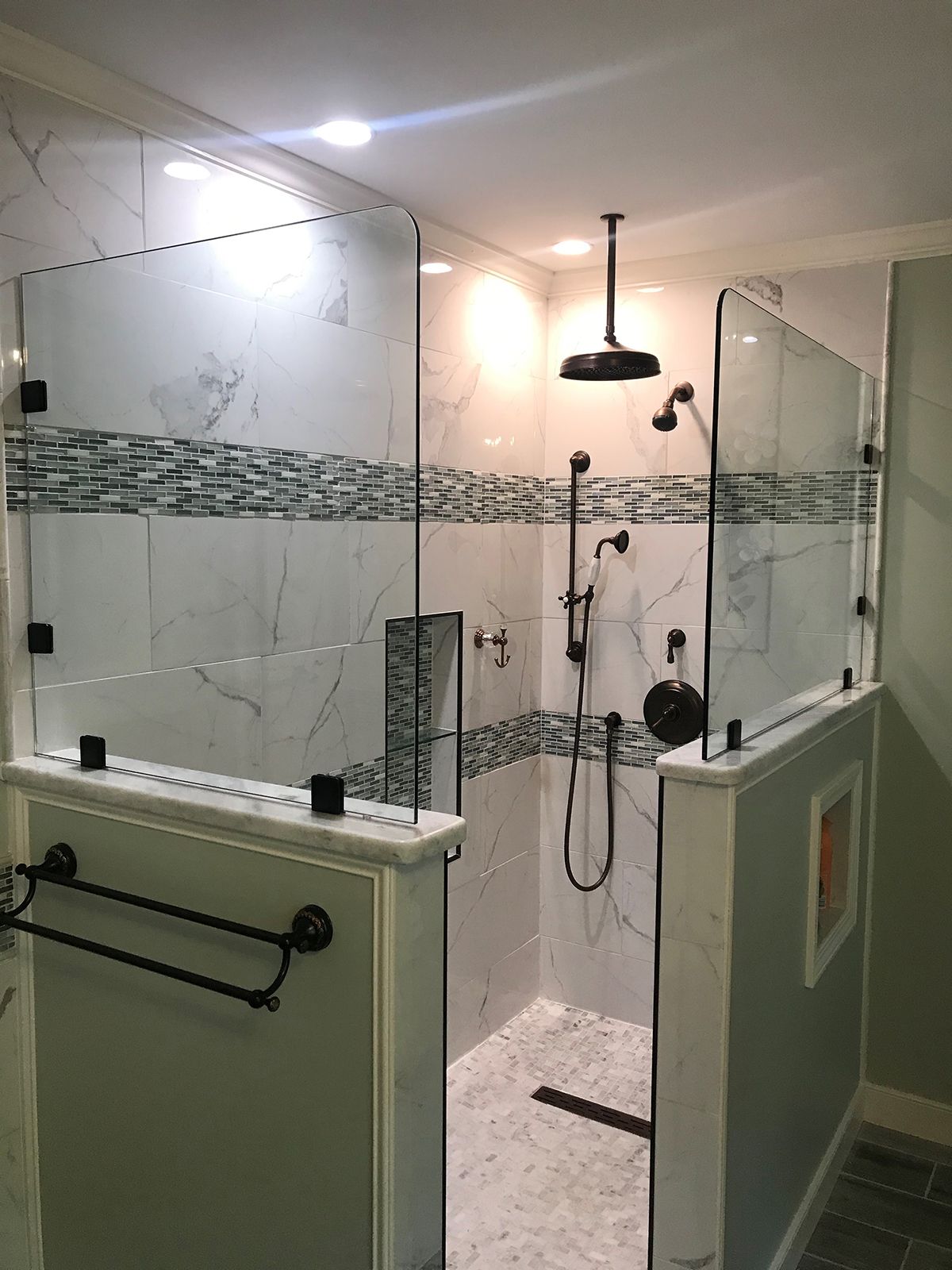 A modern walk-in shower with white marble-patterned tiles, glass panels, black fixtures, and a dual-head shower system.