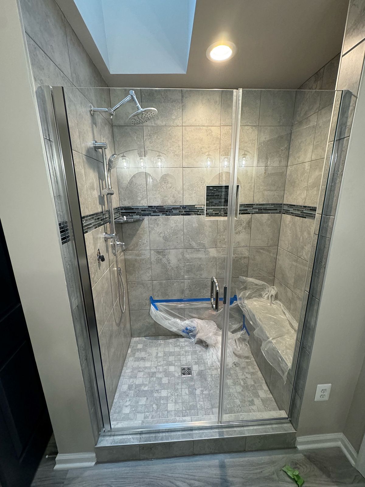 A modern glass-enclosed shower with gray tiled walls, a built-in stone bench, and a brushed nickel rainfall showerhead.